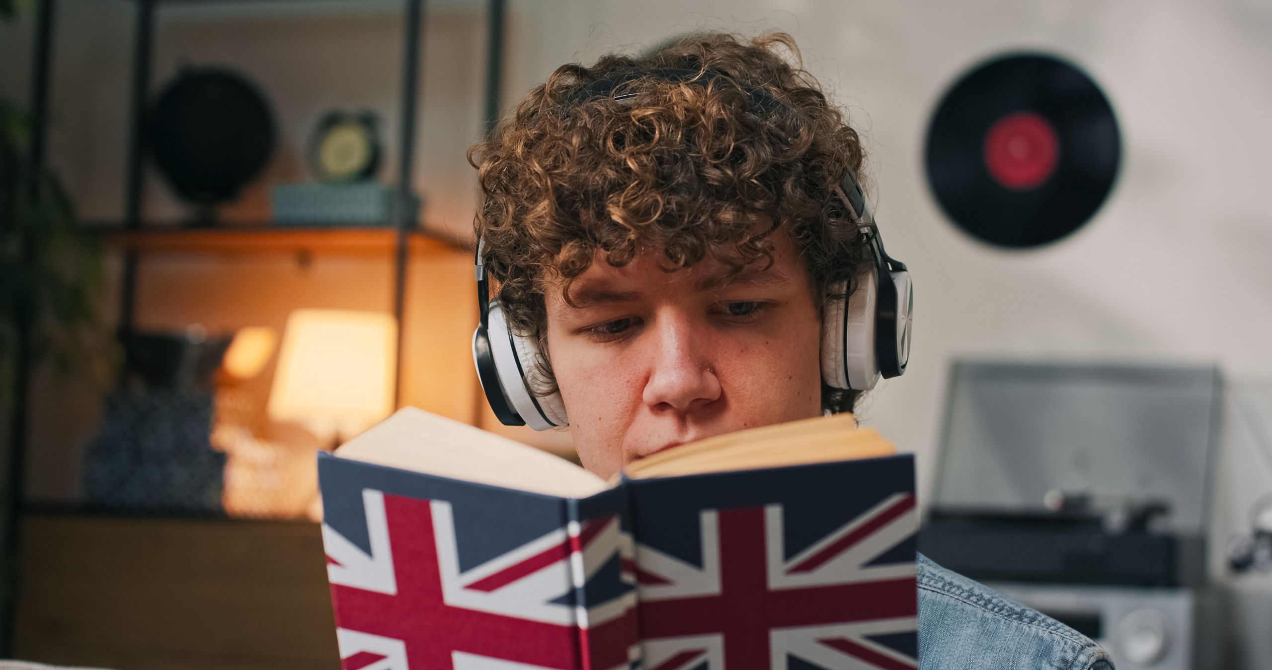 A young man sits on the sofa at home, studying a new language alone after school to prepare for a college exam.